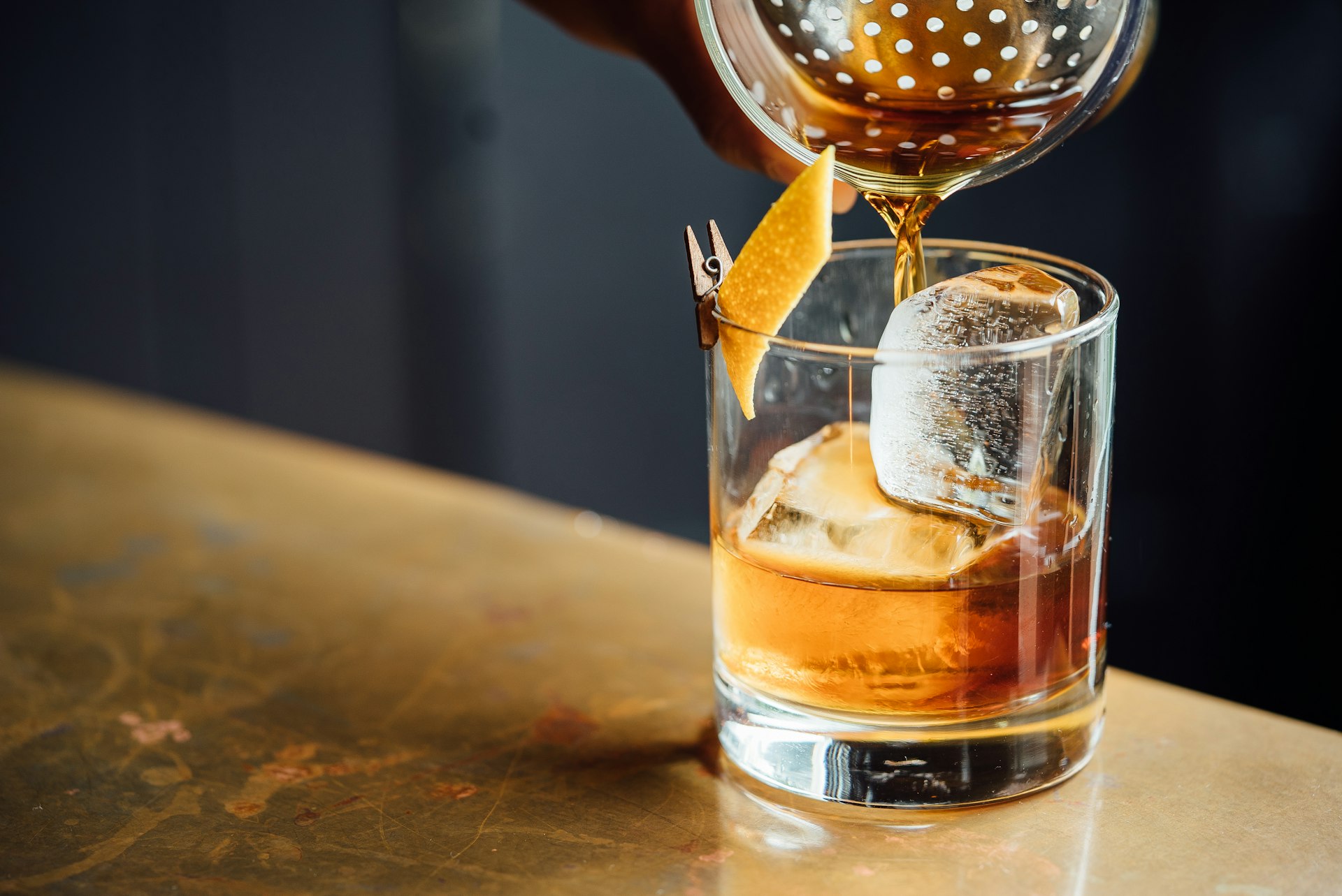 Bartender straining a craft old fashioned over ice at a dimly lit bar